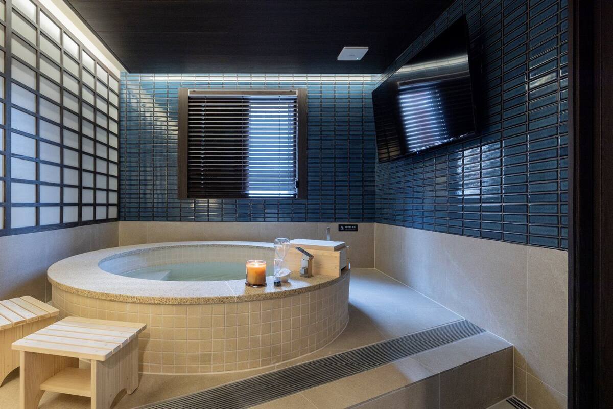 A modern bathroom with a freestanding bathtub, wooden benches, and a glass partition.