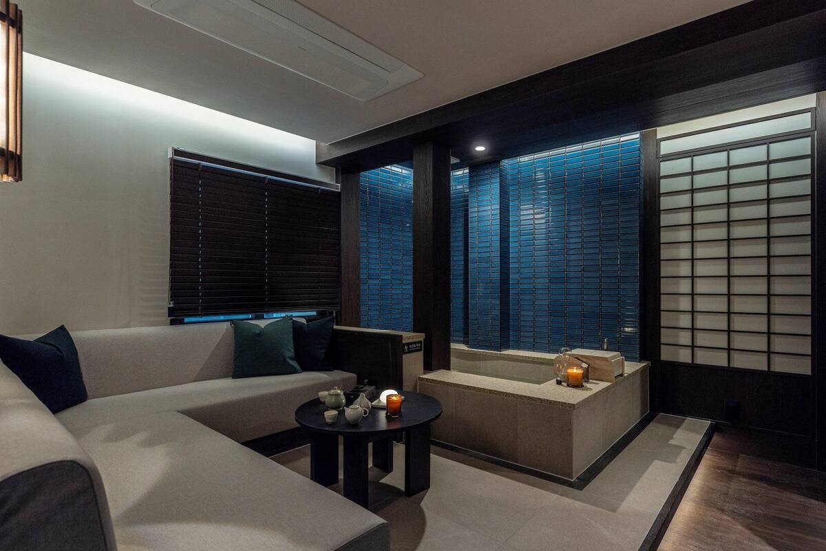 A modern living room with a sofa, a coffee table, and a small seating area with cushions.