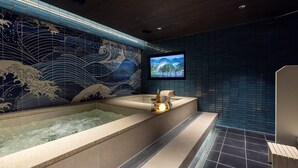 A modern bathroom with a large bathtub, a television mounted on the wall, and a decorative blue wave pattern on the wall. - Stay Passport Okinawa Ryokan Bupyeong Incheon (Incheon)