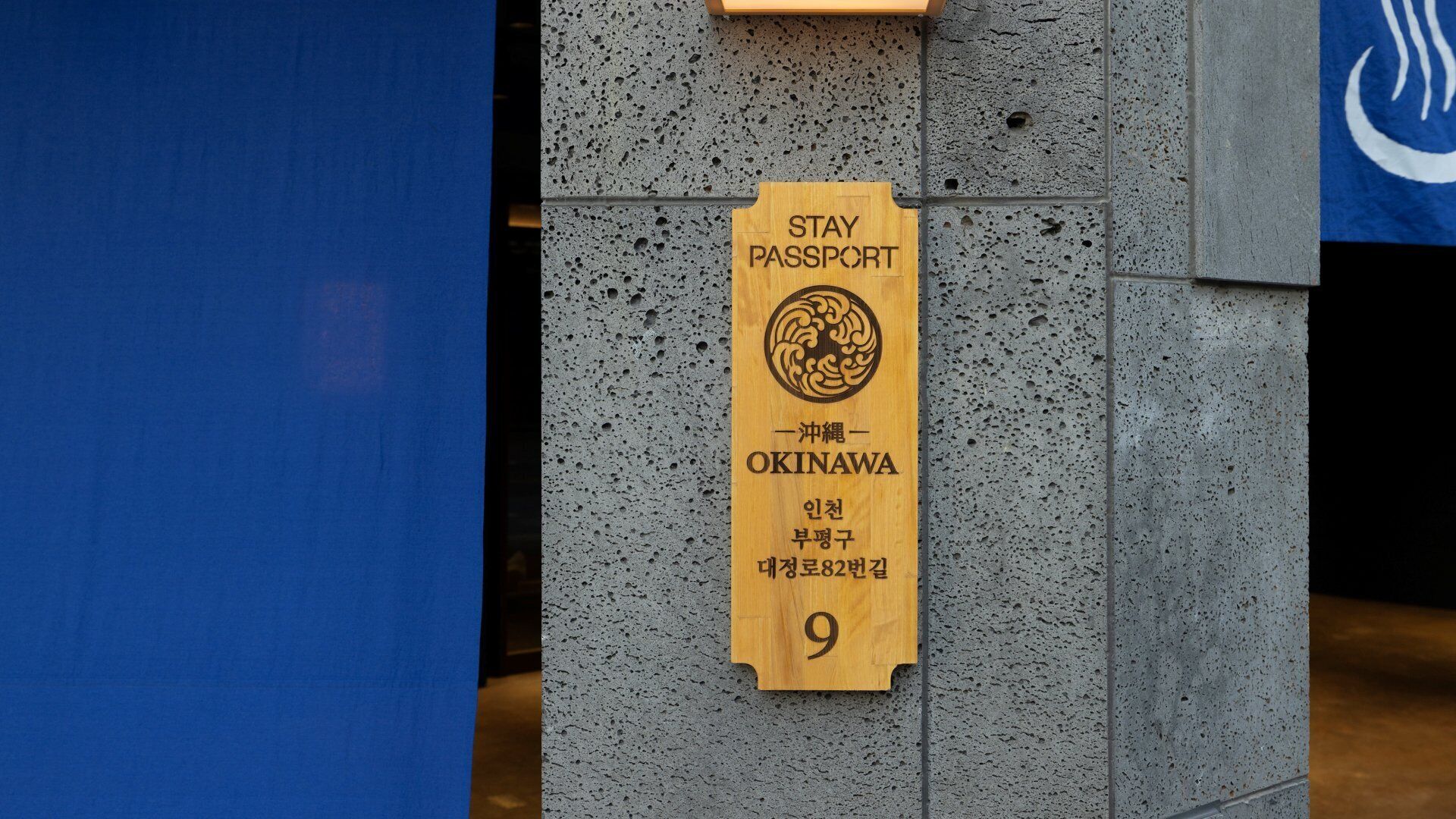 A wooden sign with "STAY PASSPORT" and "OKINAWA" on a textured wall.