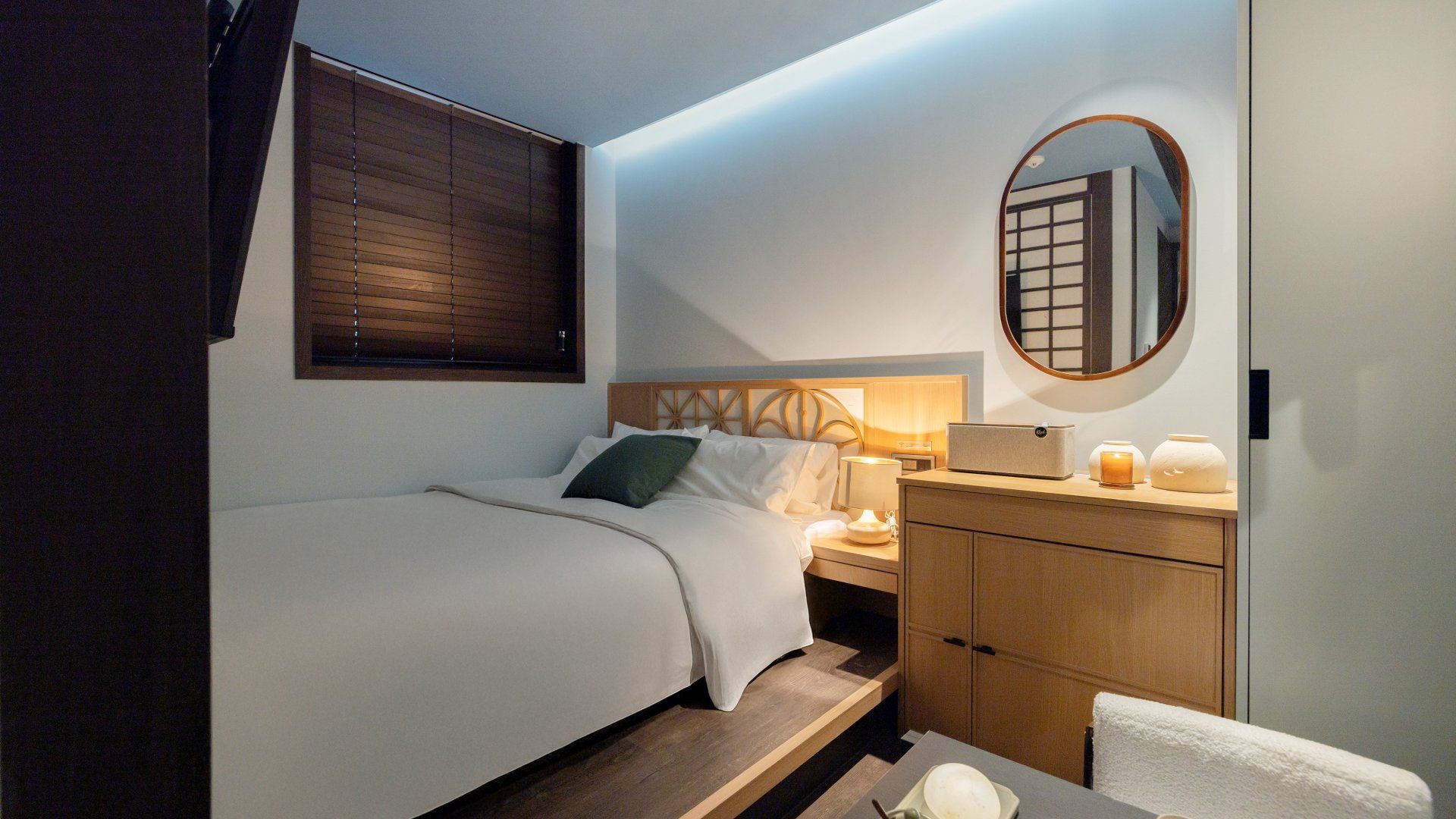 Een kleine hotelkamer met een eenpersoonsbed, nachtkastje en een klein houten kastje.