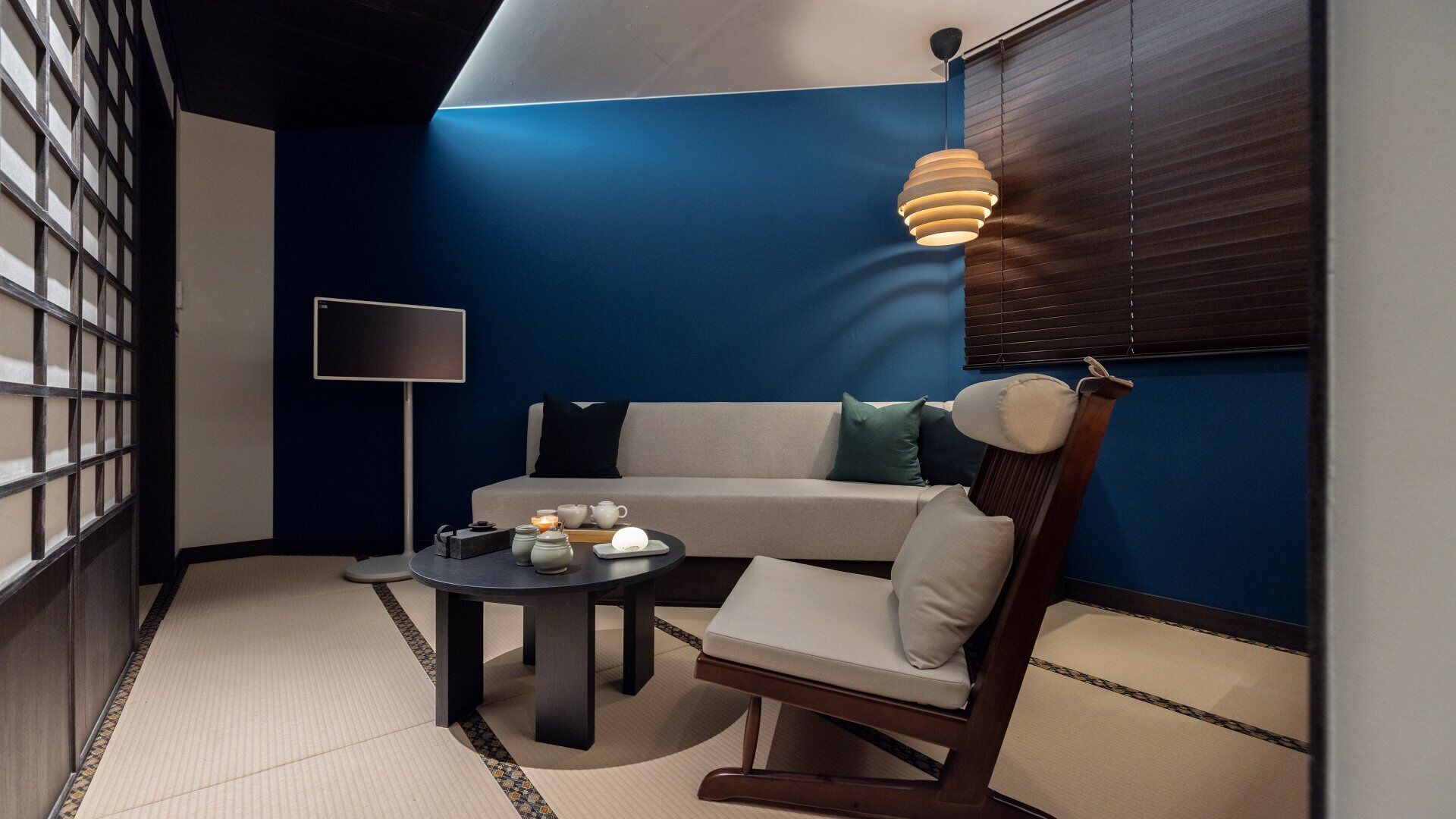 A modern room with a blue accent wall, a sofa, a chair, a small table with tea set, and a floor lamp.
