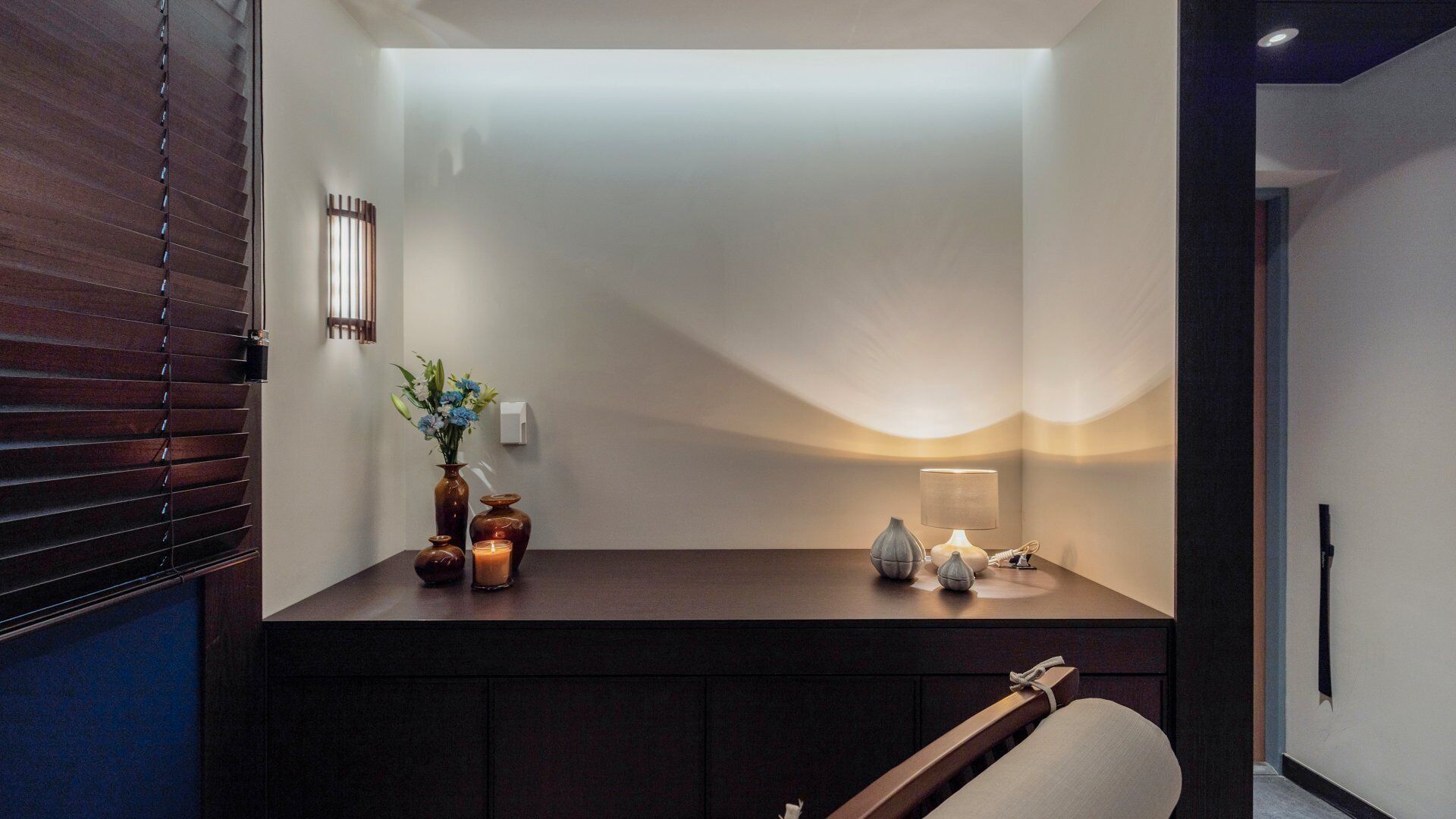 A modern room with a dark wooden desk, a vase with flowers, a candle, and a lamp.