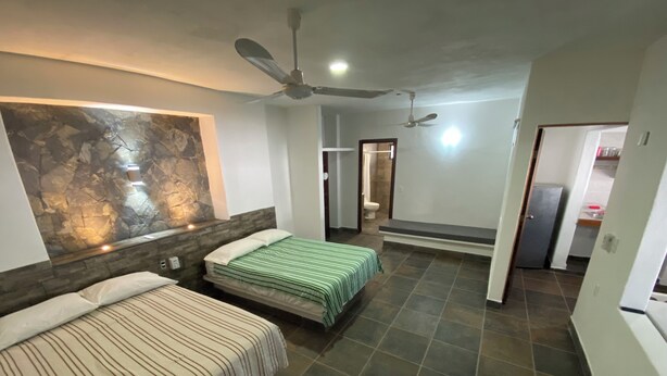 A bedroom with two beds, a stone accent wall, a ceiling fan, and a bathroom visible through an open door.