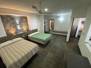 Une chambre avec deux lits, un mur décoratif en pierre, un ventilateur de plafond et une salle de bain visible à travers une porte ouverte.