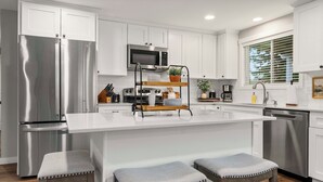 Une cuisine moderne dotée d’appareils électroménagers en acier inoxydable, d’un îlot central avec des tabourets et de meubles de rangement blancs.