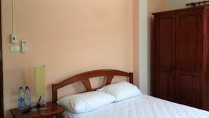 Een hotelkamer met een houten bed, een nachtkastje met waterflesjes, een lamp en een kledingkast.