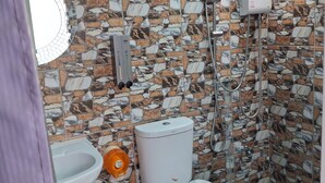 Een badkamer met een wand betegeld met een stenen mozaïek, een toilet, een bidet en een douche.