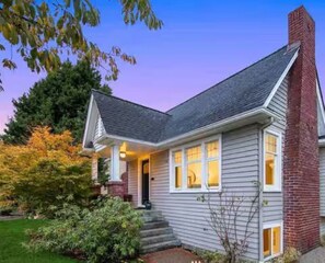 A two-story house with a gabled roof, a brick chimney, and a front porch with steps. - 5 min to UW and U-Village / Cozy Design (Seattle)