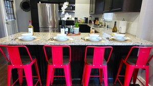 Una cocina con encimera de granito, cuatro taburetes rojos, un refrigerador de acero inoxidable y un horno negro.