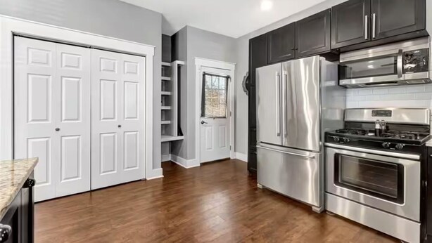 Una cocina con puertas dobles blancas, armarios oscuros, electrodomésticos de acero inoxidable y piso de madera.