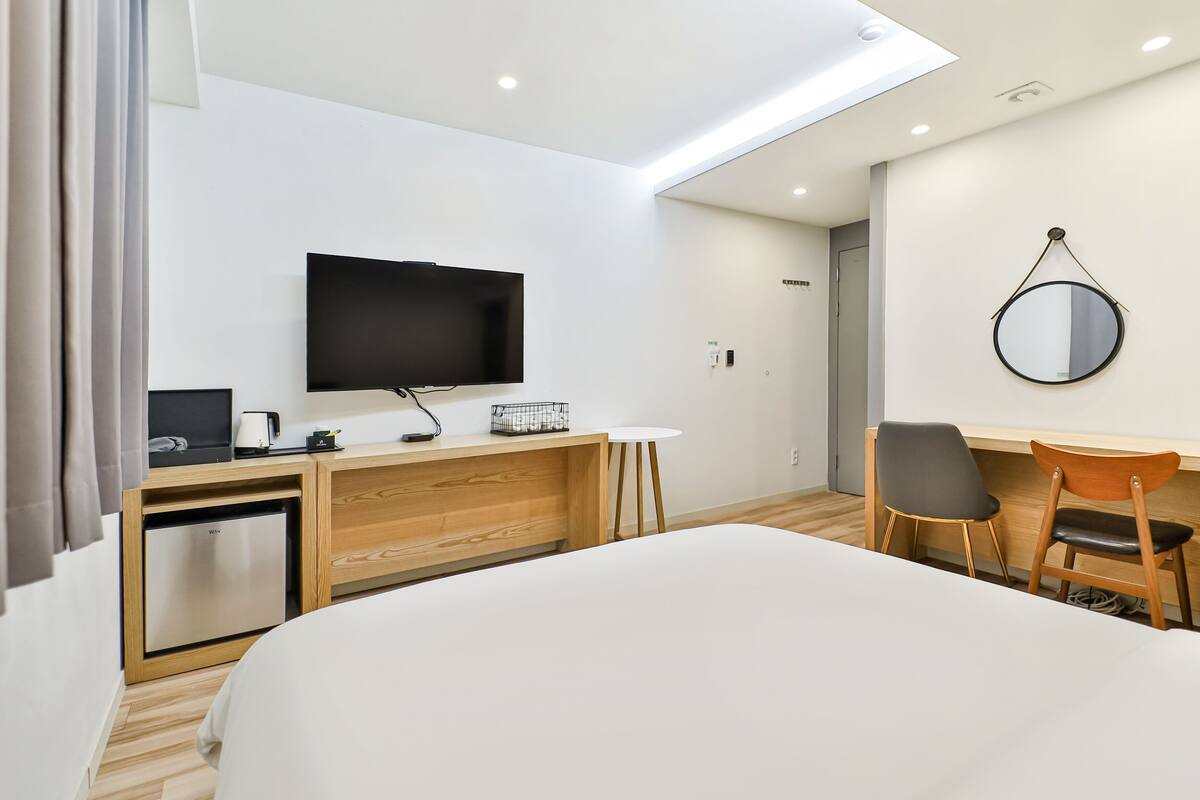 A modern hotel room with a bed, a desk, a chair, a television, and a small refrigerator.