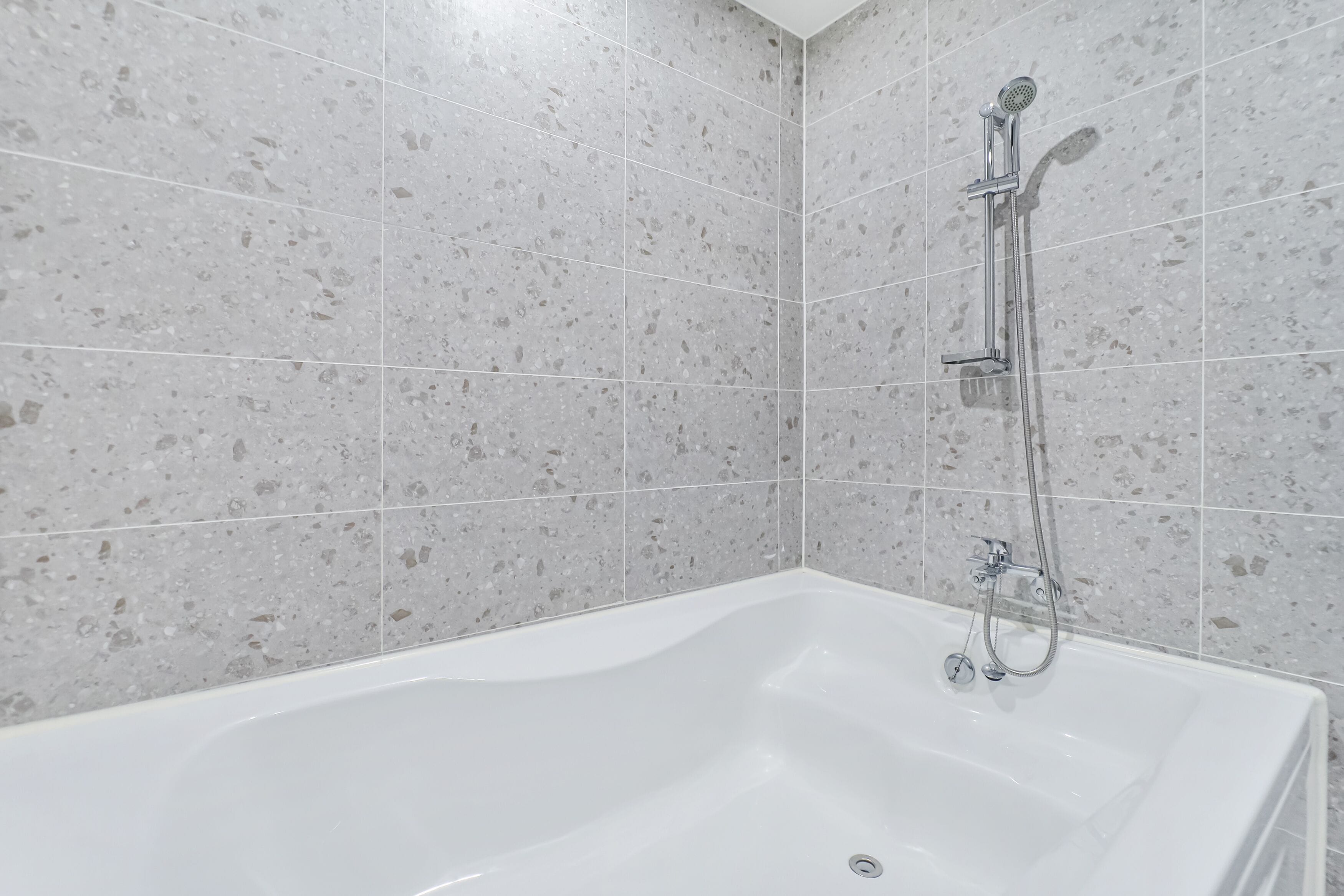 Een moderne badkamer met een vrijstaand bad, een handdouche en een wandmengkraan.