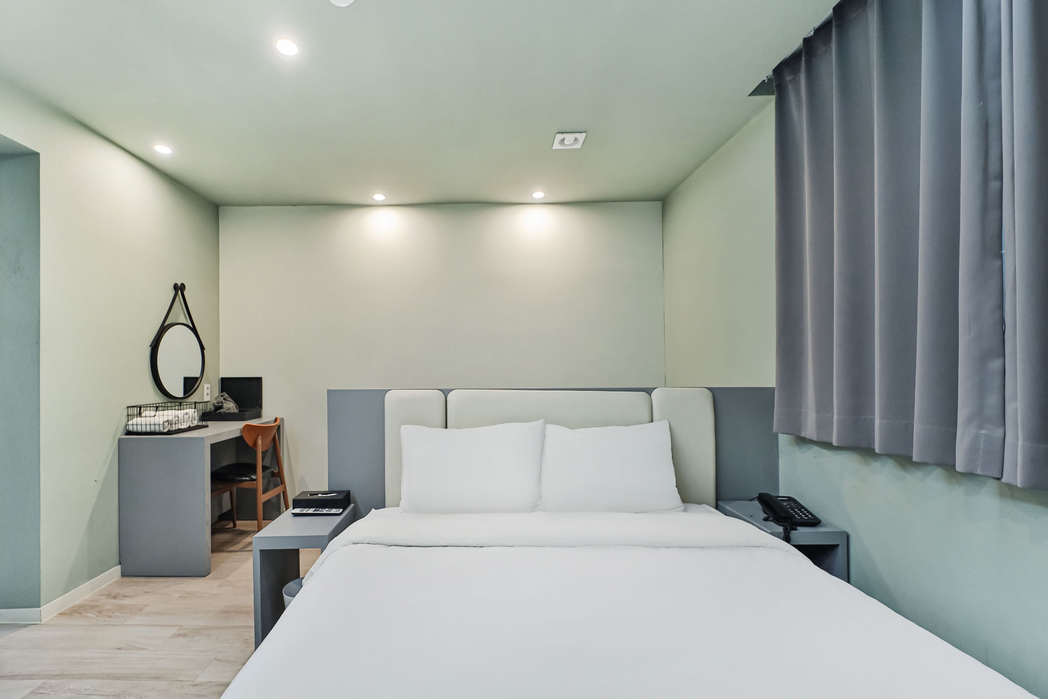 A hotel room with a bed, a desk, a chair, a mirror, and a telephone.