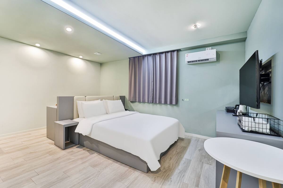 A modern hotel room with a bed, bedside table, and a small desk with a chair.