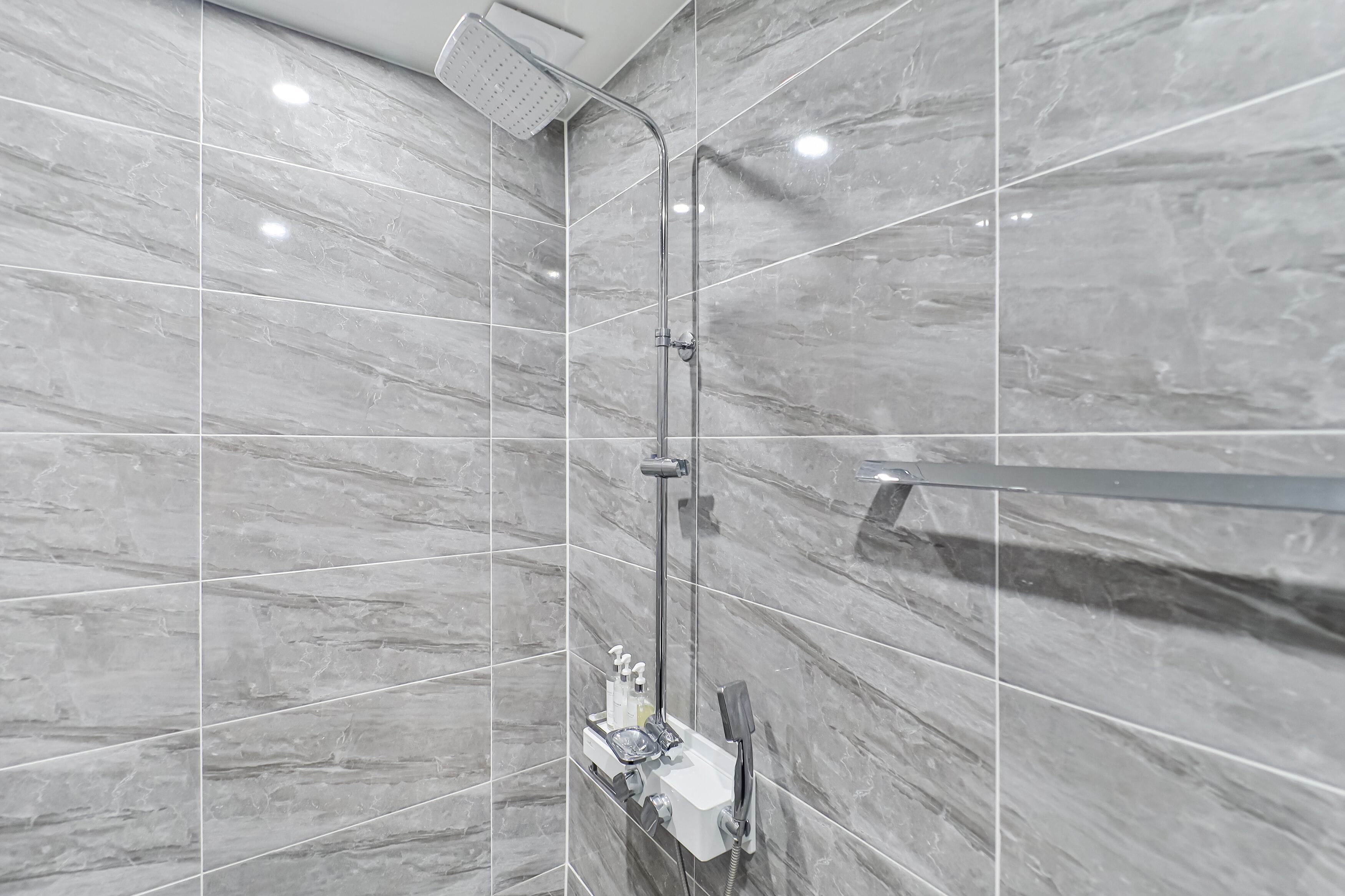 A modern bathroom with a shower, marble tiles, and a vanity with toiletries.