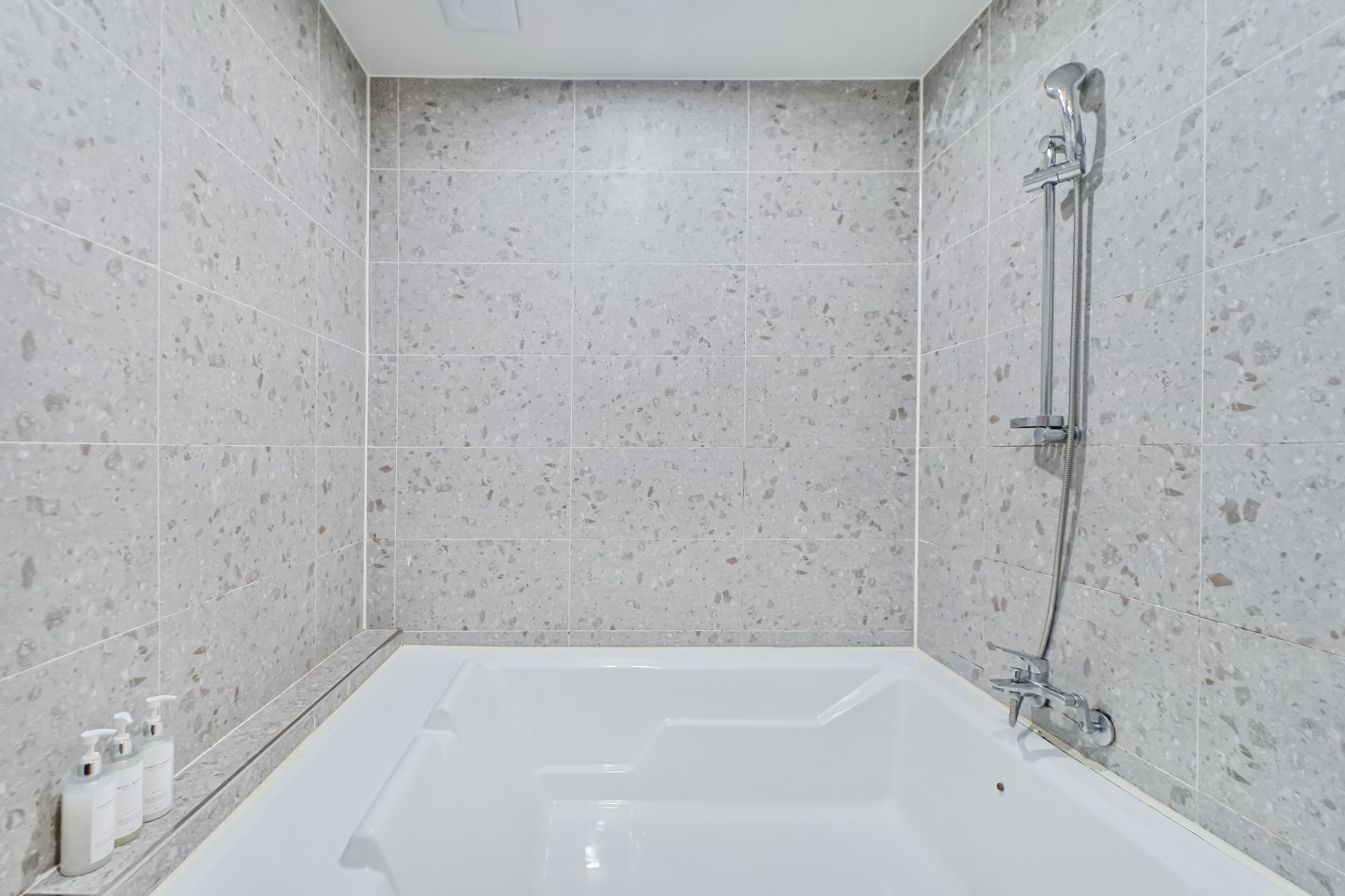 A modern bathroom with a freestanding bathtub, a handheld showerhead, and a shelf with toiletries.