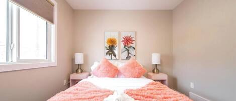 Een slaapkamer met een bed, twee nachtkastjes, een raam en twee aan de muur hangende schilderijen.