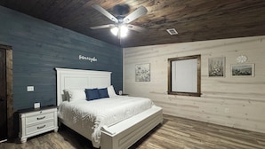 Un dormitorio con cama, mesitas de noche, ventilador de techo y paredes de madera.