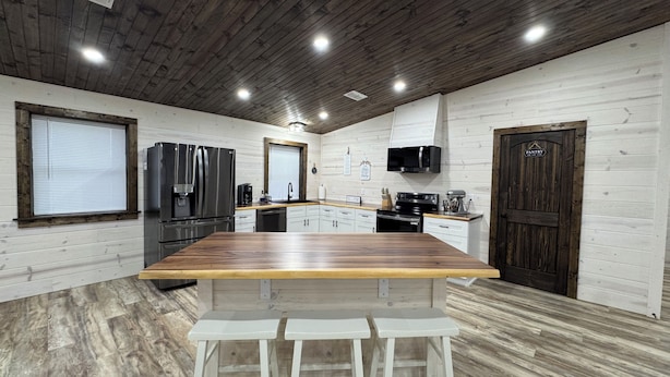 Una cocina moderna con una isla central, taburetes blancos, suelo de madera y techo de madera.
