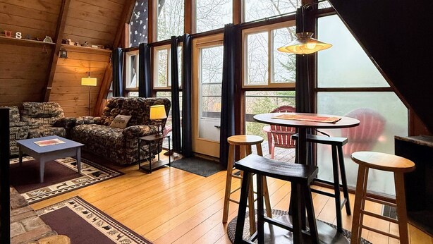 Um quarto acolhedor estilo loft com pé direito alto, vigas de madeira, uma janela grande, lareira e um espaço de jantar com banquetas.