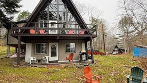 Uma casa moderna com uma varanda ampla, várias cadeiras Adirondack e um poço de fogo no quintal.