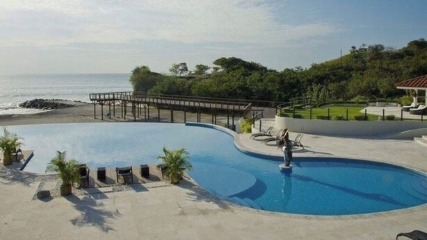 Piscina com vista para o oceano, um deck de madeira e cadeiras de descanso.