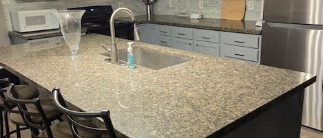 A kitchen with granite countertops, stainless steel appliances, and a central island with bar stools.