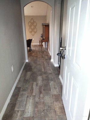 A hallway with a wooden floor, a door on the right, and a chair in the background. - Houston Family Getaway | Parking & WiFi Included! (Houston)