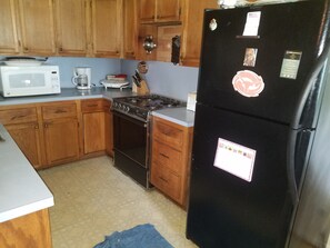 A kitchen with wooden cabinets, a black refrigerator, a white microwave, and a stove. - FIFA Friendly - Large Groups Allowed (Houston)