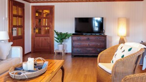 A cozy living room with wooden ceiling beams, a television on a dresser, wicker furniture, and a lamp. - Les Agettes 1865 by Interhome (Les Mayens-de-Sion)