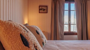 A bedroom with a large bed, a window with curtains, and a framed picture on the wall. - Les Agettes 1865 by Interhome (Les Mayens-de-Sion)
