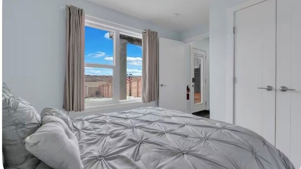 A bedroom with a large bed, a window with curtains, a door, and a view of the outside. - Newly Built Guesthouse Suite (Calgary)