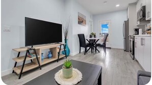 A modern living room with a flat-screen TV on a wooden stand, a dining area with a table and chairs, and a kitchen with white cabinets and appliances. - Newly Built Guesthouse Suite (Calgary)
