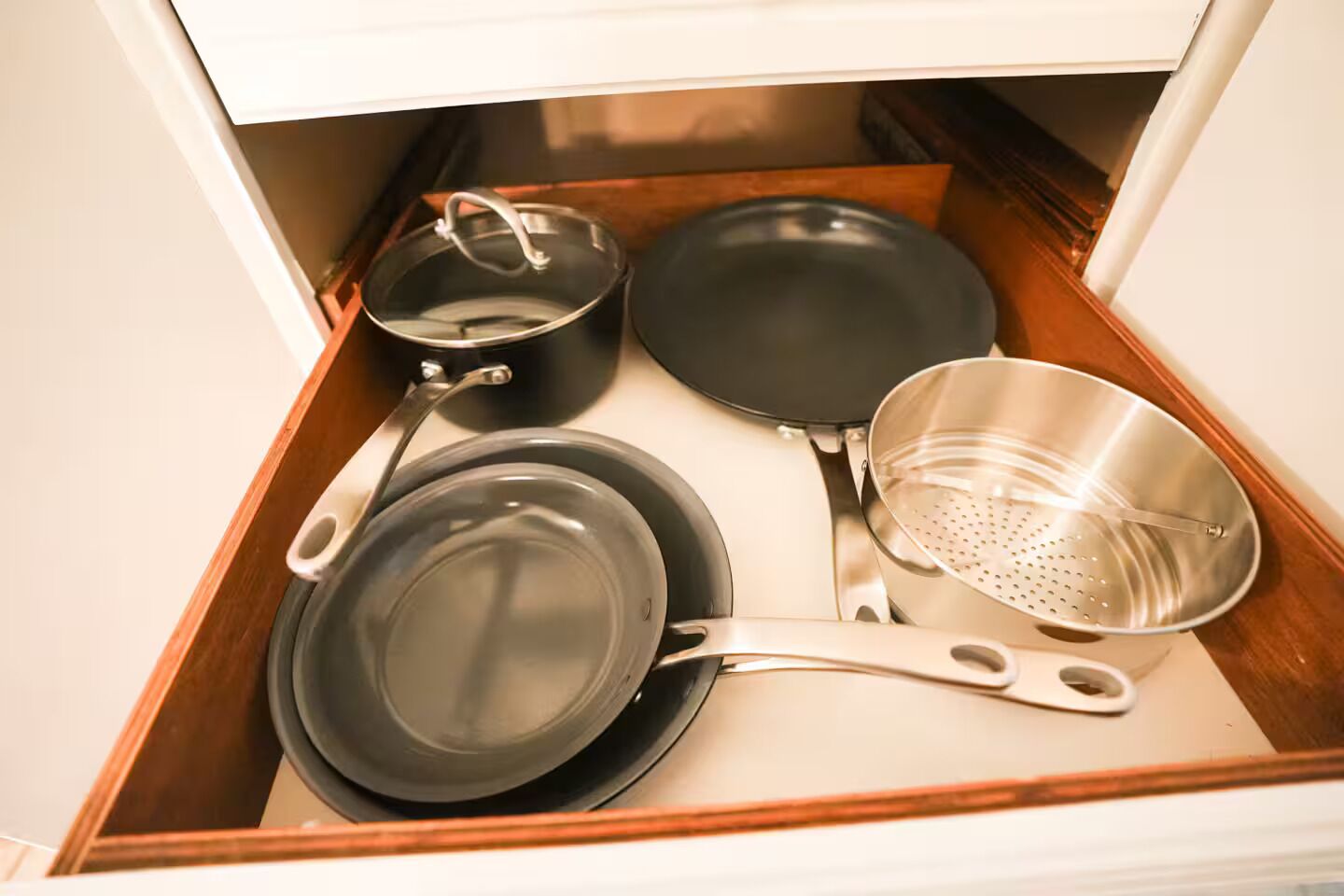 A drawer containing a frying pan, a pot, a pan, and a colander.