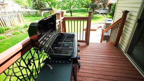 A barbecue grill on a wooden deck with a view of a backyard and a house.