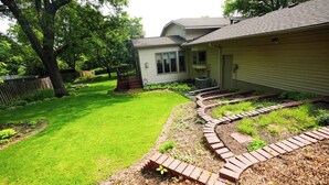 A residential backyard with a well-maintained lawn, a brick pathway, and a house with a front porch.