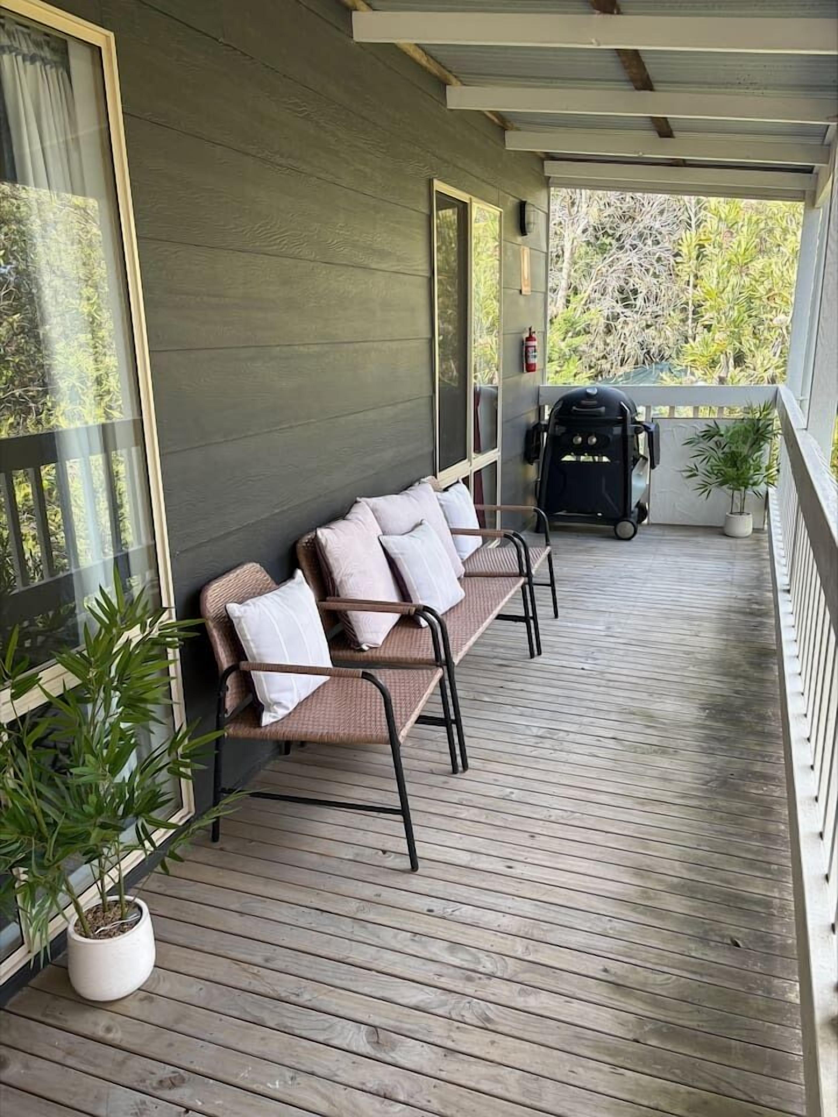 A covered porch with a bench and a barbecue grill.