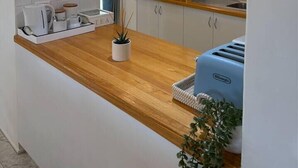 Een moderne keuken met houten aanrecht, een ingebouwde magnetron en een broodrooster. Er staat een kleine plant op het aanrecht en een raam met gordijnen.