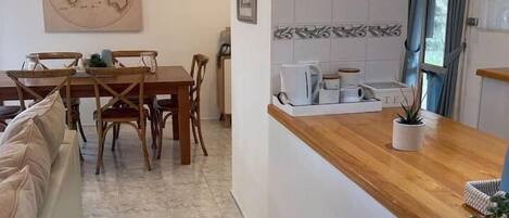 A compact kitchen with a wooden countertop, a dining area with a table and chairs, and a tiled floor.