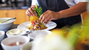 Ein Koch bereitet ein Gericht mit Nudeln, Gemüse und Fleisch zu.