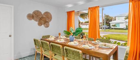 Un comedor con una larga mesa de madera dispuesta para cuatro personas, rodeada de sillas con cojines verdes.