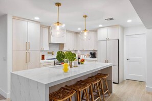 A modern kitchen with white cabinetry, a marble countertop, and a central island with bar stools. - Wellness Retreat at WPB - HotTub | Sauna | ColdPlunge | Golf (West Palm Beach)
