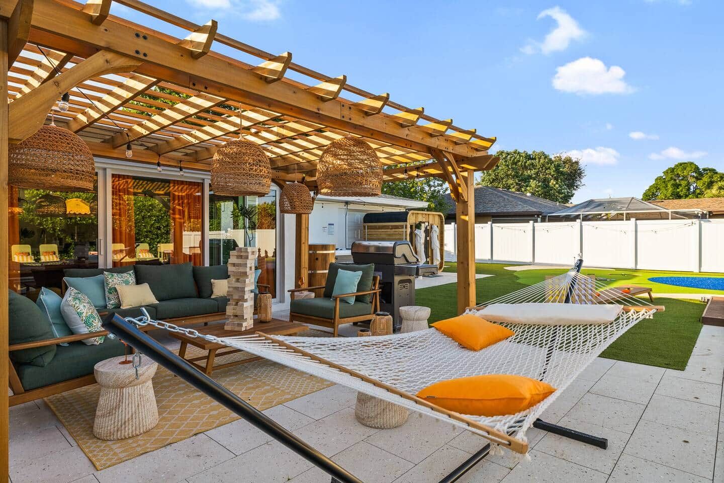 Un área de estar al aire libre techada con una parrilla, una hamaca y una piscina al fondo.