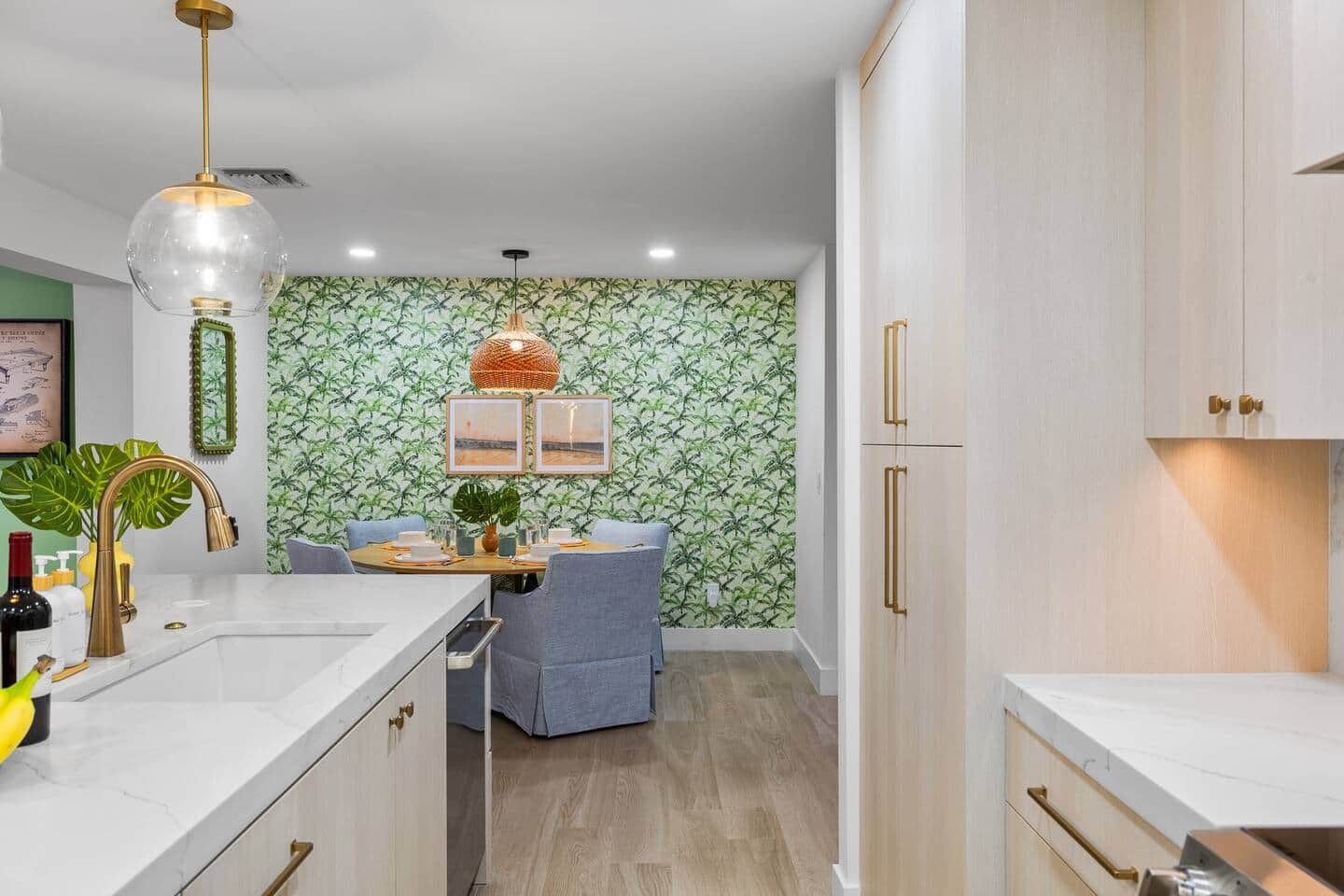 Una cocina moderna con armarios blancos, una zona de comedor con una silla azul y una pared con estampado de hojas.