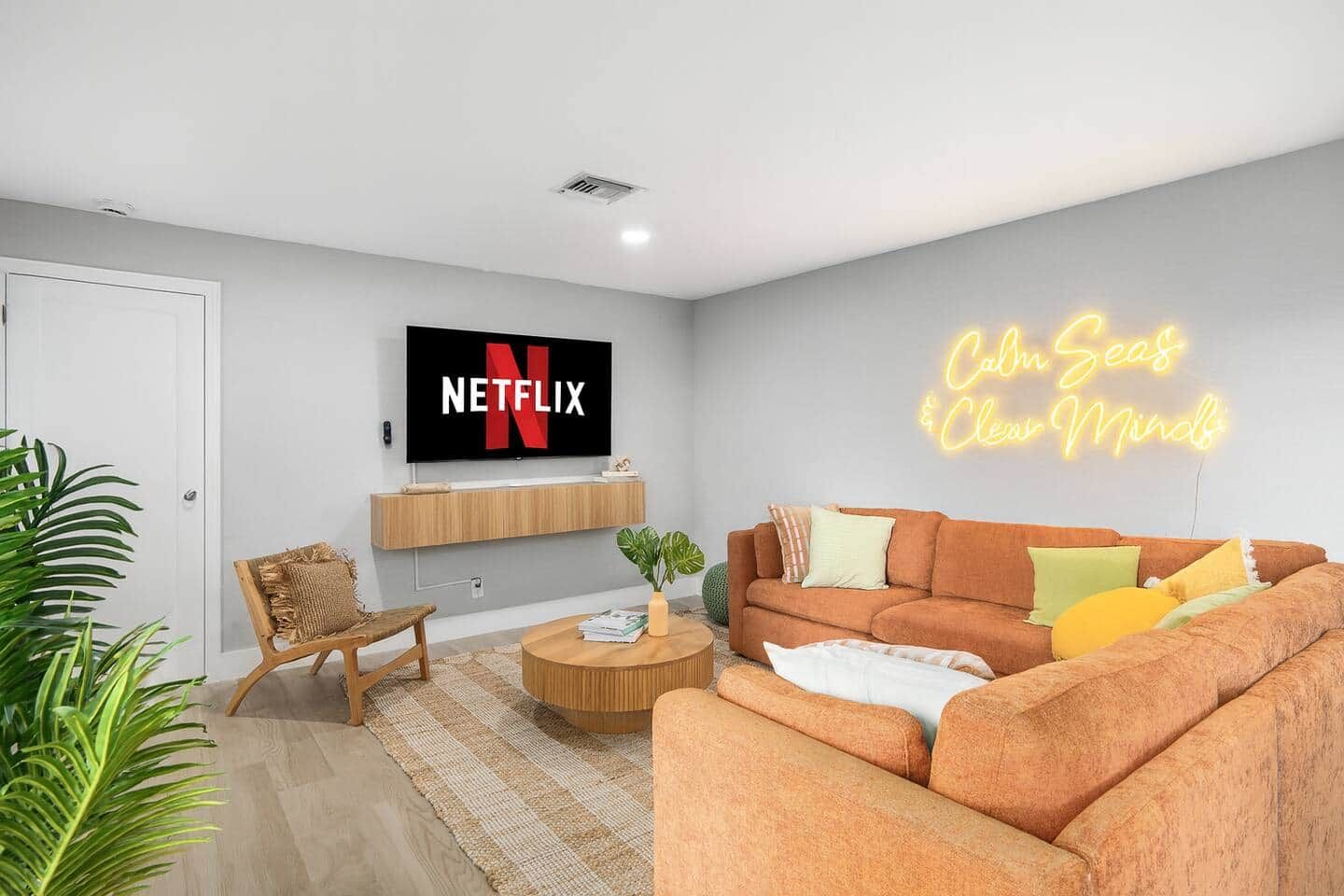 Un salon moderne avec un téléviseur connecté à Netflix, un néon, un canapé, une table basse et un fauteuil.