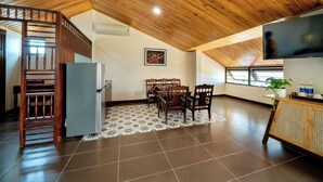 A spacious room with a wooden ceiling, a dining area with chairs and a table, a refrigerator, a TV, and a window with a view. - Virgo Villa Que Hoi An (Hoi An)