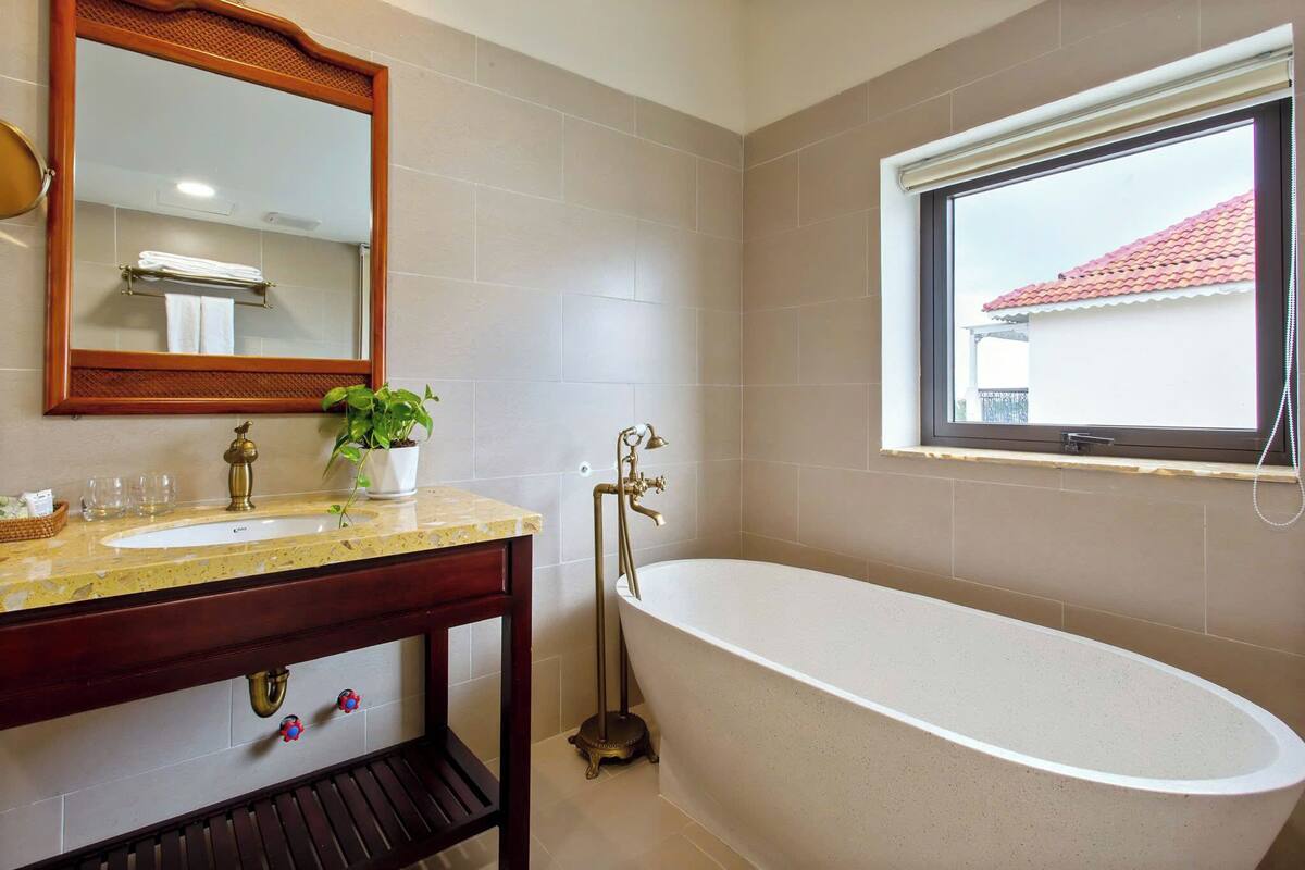 Une salle de bain avec une baignoire sur pieds, un lavabo avec un miroir au-dessus et une fenêtre donnant sur un bâtiment avec un toit rouge.