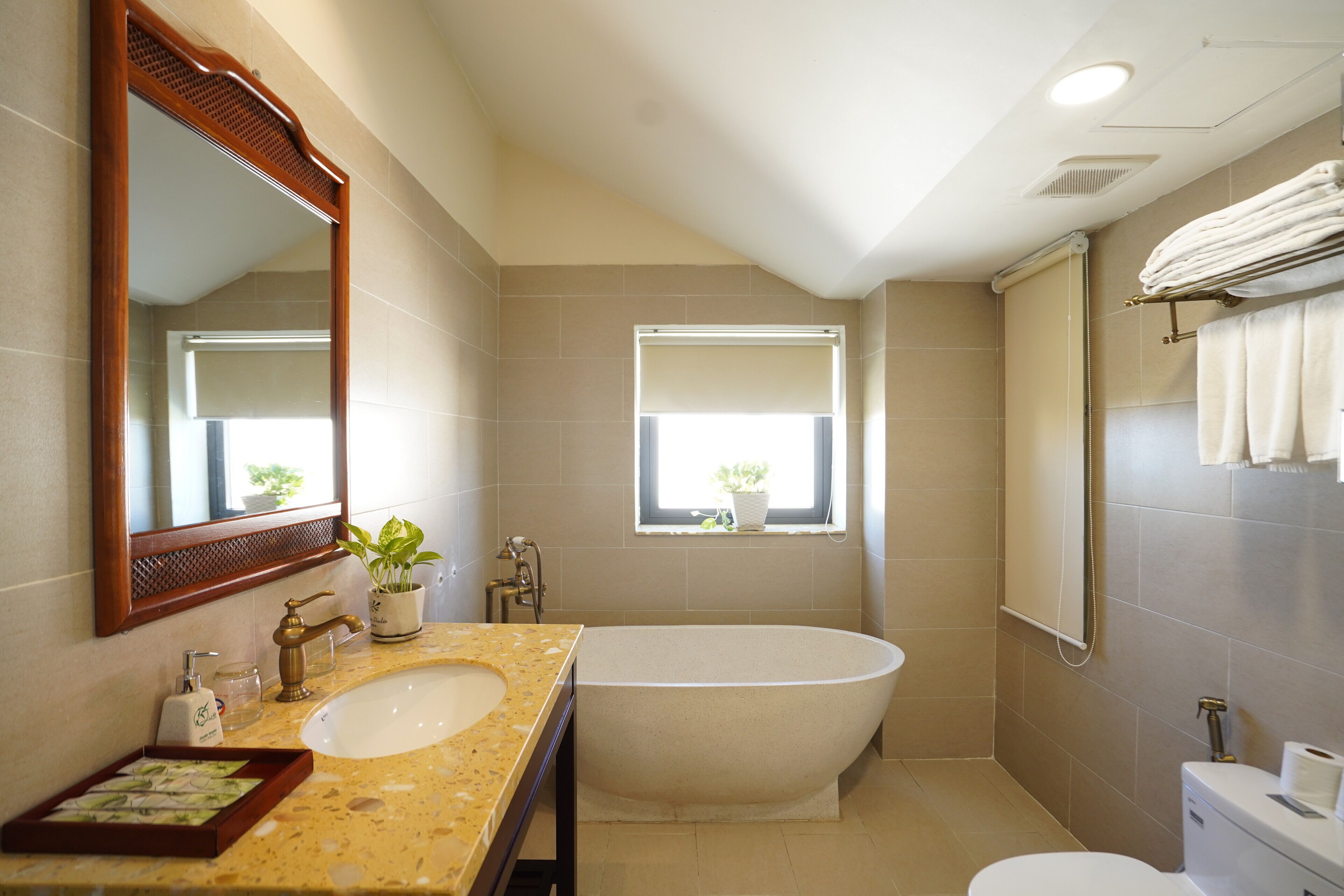 A bathroom with a freestanding bathtub, a sink, a mirror, and a window with a view of greenery outside.