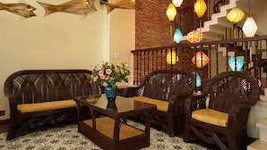 A living room with wicker furniture, a glass coffee table, and a vase of flowers. - Virgo Villa Que Hoi An (Hoi An)